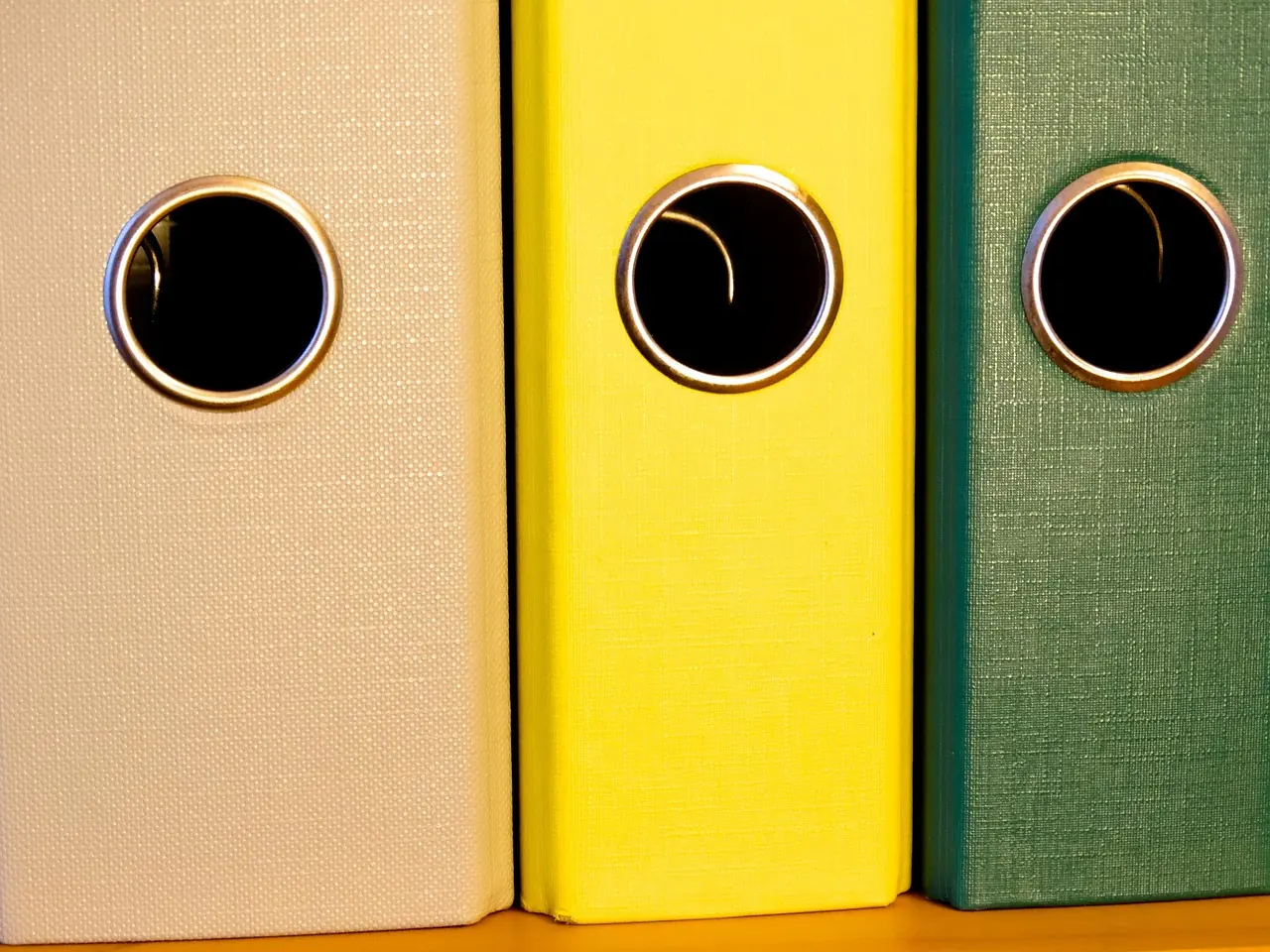 Trois classeurs à levier beige, jaune et vert alignés sur une étagère