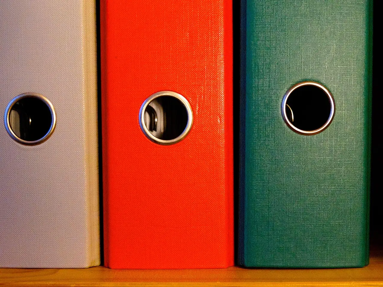 Classeurs beige, rouge et vert rangés côte à côte, vus de près